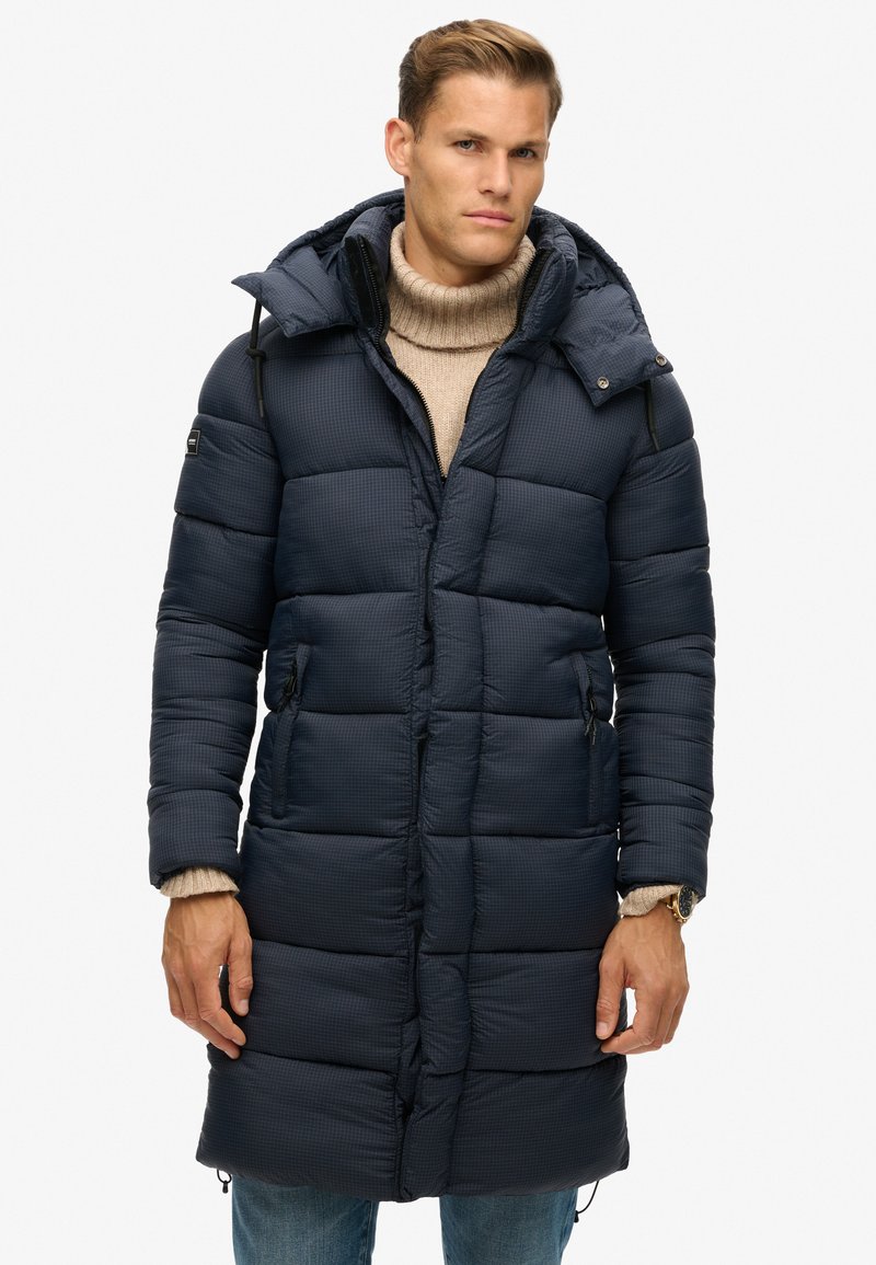 Marineblå dunjakke med hætte, quiltet design, lynlåslommer og snøre detaljer. Blødt stof med en glat tekstur.