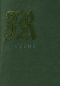 Tessuto di cotone verde con un logo verde in rilievo "JR" e la scritta "JOHN RICHMOND" in un carattere blu a contrasto.