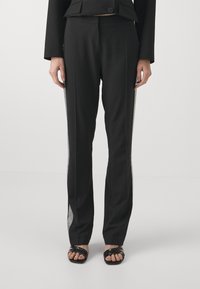 Black trousers with a tailored fit, featuring textured mesh side panels and a smooth fabric finish. Paired with black strappy sandals.