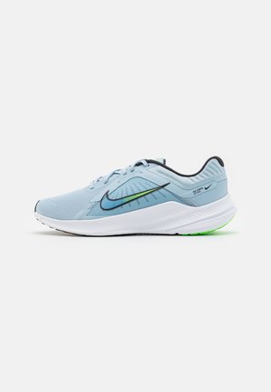 Chaussure de course Nike bleu clair avec swoosh noir et vert, semelle blanche et bordure noire, vue de côté sur fond blanc.