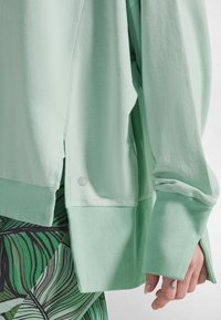 Vaaleanvihreä collegepaita, jossa on ribbineulostekstuuri, pitkät hihat, sivuhalkiot ja hieman ylisuurikokoinen istuvuus. Varustettu hienovaraisella logodetaljilla.