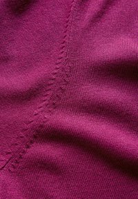 Gros plan sur un tissu tricoté magenta avec une couture visible et des détails de points fins montrant la texture et le motif de tissage.