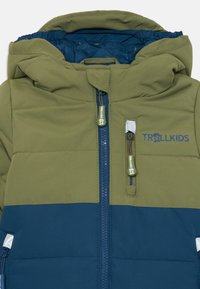 Veste à capuche pour enfants avec une partie supérieure en vert olive, une partie inférieure en bleu marine, fermeture éclair à l'avant, poche zippée sur la poitrine et logo "TROLLKIDS" sur la poitrine.