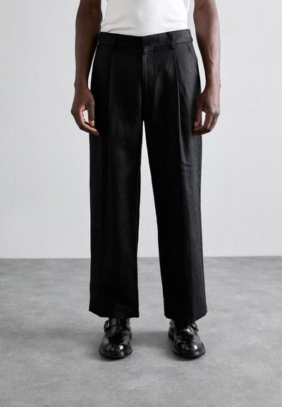 Schwarze Leinenhose mit lockerer Passform und flachem Bund, ausgestattet mit doppelten Falten und glatter Textur, kombiniert mit polierten schwarzen Schuhen.
