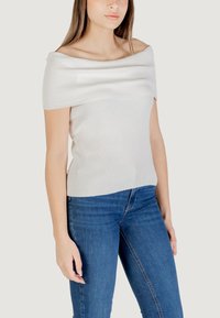 Top a spalle scoperte in maglia a coste di colore grigio chiaro, con una ampia scollatura drappeggiata e un corpo aderente, abbinato a jeans di denim blu scuro.