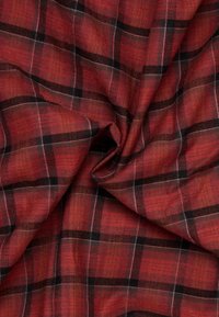 Tessuto a quadri rosso e nero con una consistenza morbida, caratterizzato da linee che si intersecano e un aspetto caldo e strutturato.