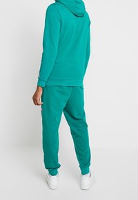 Turkos hoodie och matchande sweatpants i mjukt tyg. Har en huva, ribbad mudd och en liten logotypdetalj på byxorna.