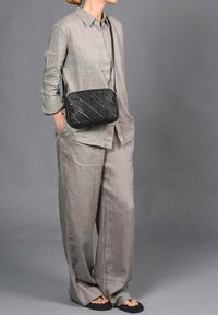 Camisa de lino gris y pantalones de pierna ancha combinados con un bolso cruzado negro de tejido, que cuenta con una textura suave y una correa ajustable.