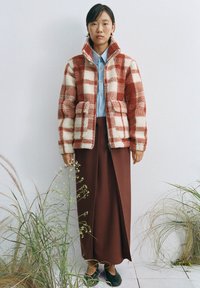 Red and white check pattern jacket made of textured material, paired with a light blue shirt and brown skirt, worn with black shoes.