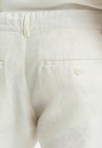 Lichtbeige linnen broek met een knoopzak aan de achterkant, een gladde textuur en een getailleerde pasvorm met minimalistische ontwerpelementen.