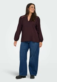 Blouse bourgogne avec des détails en dentelle sur les épaules, associée à un jean bleu à jambe large. La tenue est complétée par des chaussures à plateforme noires.