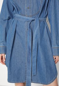 Denim shirt dress with a belted waist, featuring long sleeves, a button-up front, and a rounded hem in a light blue shade.