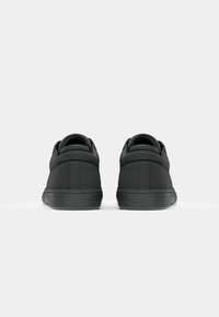 Black sneakers with a smooth texture, round toe, and padded collar. Features a grooved sole for traction and minimalist design.