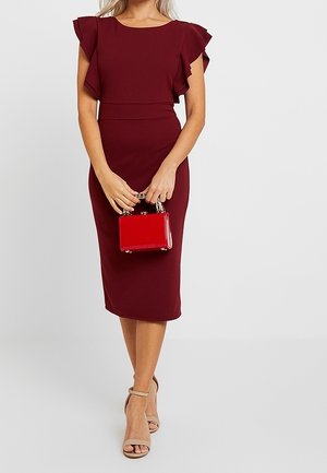 Robe cintrée bordeaux avec manches à volants, associée à un petit sac à main rouge. Le mannequin porte des sandales à talons beiges. Texture de tissu lisse.