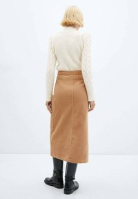 Maglione a trama cable cream con maniche lunghe abbinato a una gonna midi in velluto a coste color sabbia e stivaletti neri, visto da dietro.