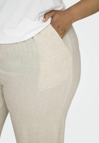 Beige linnen broek met een gladde textuur, voorzien van zijzakken en een getailleerde pasvorm, aangevuld met een wit shirt nabij de taille.