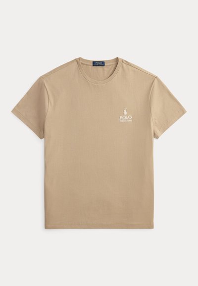 Μπεζ βαμβακερό μπλουζάκι με στρογγυλή λαιμόκοψη και κοντά μανίκια. Διαθέτει έναν λευκό κεντητό λογότυπο στο αριστερό στήθος. Ομαλή υφή.