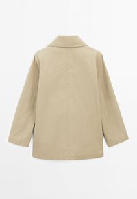Veste beige à manches longues avec col, présentée de dos sur un fond blanc uni.