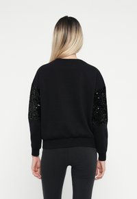 Sweatshirt preto com detalhes em lantejoulas nas mangas, apresentando um decote redondo clássico e punhos e bainha em malha. Textura suave.