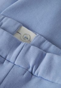 Svetlo modra tkanina z teksturirano površino; ima elastičen pas s prozornim gumbom in belim notranjim etiketom.