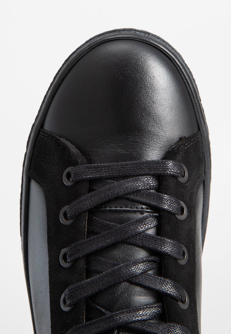Czarny sneaker wykonany z gładkiej skóry i teksturowanej zamszowej tkaniny. Posiada okrągłe czarne sznurowadła, zaokrąglony czubek oraz subtelne detale przeszycia.