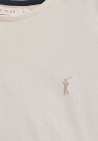 Lichtbeige T-shirt met korte mouwen en een ronde halslijn van zachte stof. Heeft een klein, metalen logo van een golfer op de linkerborst.