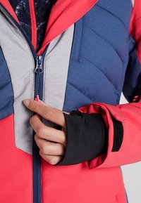 Gepolsterte Jacke in Rot, Navy und Grau mit durchgehendem Reißverschluss. Verfügt über Daumenlöcher an den Bündchen und ein strukturiertes, isoliertes Futter für Wärme.