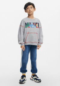 Harmaa huppari, jossa on "MARVEL" -logo, punaiset tikkaukset ja etutasku. Siniset farkkumaista kangasta joggerit, joissa on harmaat sivupaneelit. Värikkäät lenkkarit.