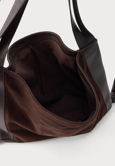 Sac d'épaule en suède marron foncé et cuir noir avec un dessus ouvert montrant une poche intérieure spacieuse et vide.