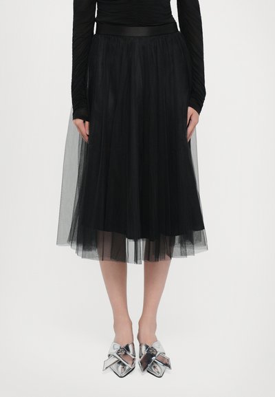 Gonna midi in tulle nera con una vita aderente, caratterizzata da un tessuto trasparente a strati e abbinata a scarpe dettagliate con un fiocco argentato lucido.