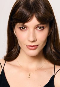 Złoty naszyjnik z zawieszką w kształcie nuty muzycznej na cienkim łańcuszku, noszony na czarnej bluzce. Gładka faktura, minimalistyczny design.