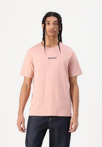 Lyserød bomulds T-shirt med korte ærmer, rund halsudskæring og navy "element" logo trykt på brystet. Båret med mørke jeans.