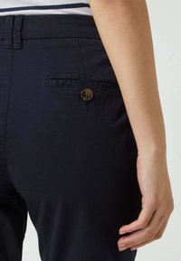 Detailní záběr osoby v tmavě námořnických kalhotách s knoflíkovou zadní kapsou a pruhovaném topu zasunutém dovnitř.