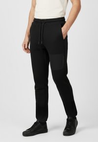 Czarne dresy o zwężanym kroju, z elastyczną talią i boczną kieszenią na zamek. Wykonane z gładkiego, elastycznego materiału.