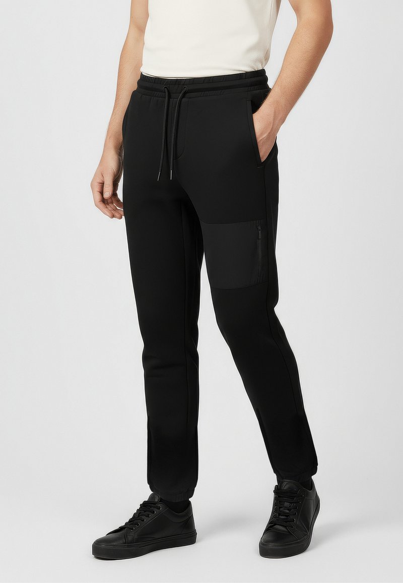 Czarne dresy o zwężanym kroju, z elastyczną talią i boczną kieszenią na zamek. Wykonane z gładkiego, elastycznego materiału.