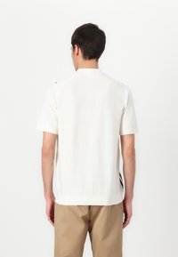 Kratke rokave, svetlo bež pletena majica z ohlapnim krojem, z rahlo rebrasto teksturo in stranskimi razporki na robu.