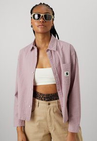 Ljusrosa, texturerad långärmad skjorta med knappar framtill och ficka. Matchad med en vit cropped topp och beige, löst sittande byxor med leopardmönstrad midja.