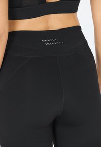 Zwarte leggings met een hoge tailleband, met een gladde textuur en horizontale reflecterende lijnen op de achterkant voor betere zichtbaarheid.