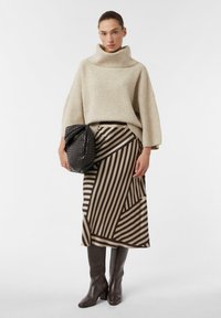 Beżowy sweter z golfem w prążki, brązowa spódnica midi w paski w kolorze kremowym, brązowe kozaki do kolan oraz czarna torebka z fakturą.