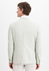 Hellgrüner Leinen-Blazer mit tailliertem Schnitt, Schlitz hinten und dekorativen Knopfakzenten an den Ärmeln. Glatte Textur.