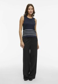 Top senza maniche blu navy con strisce orizzontali bianche sull'orlo, abbinato a pantaloni neri larghi. Texture liscia e vestibilità comoda.