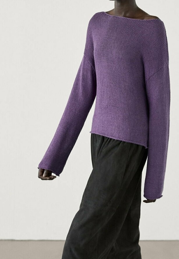 Pull en maille violet avec un large décolleté et des manches longues, accompagné d'un pantalon sombre et ample. Tissu texturé avec une coupe décontractée.