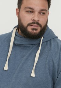 Sudadera azul con cuello tipo embudo, cordones crema y una textura suave, con un ajuste relajado y mangas raglán.