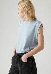 Top senza maniche di colore blu chiaro con scollo rotondo, texture liscia e vestibilità casual, abbinato a pantaloni neri a vita alta con cintura da annodare.