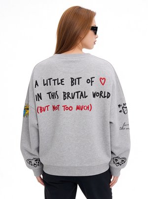 Personne aux longs cheveux châtain clair portant des lunettes de soleil noires et un sweat-shirt gris avec un texte et des dessins ludiques au dos et sur les manches.