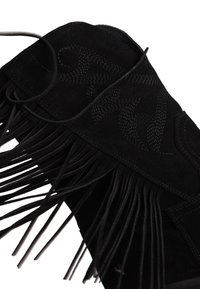 Μαύρο μποτάκι από σουέντ με κεντητά σχέδια και μακριά κρόσσια κατά μήκος του κορμού, τοποθετημένο σε λευκό φόντο.