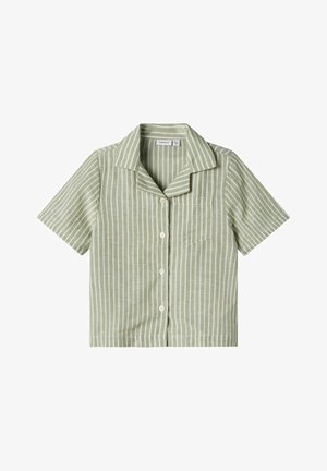 Camicetta a maniche corte di verde chiaro con righe verticali bianche, chiusura frontale con bottoni e una tasca sul petto. Realizzata in tessuto morbido.