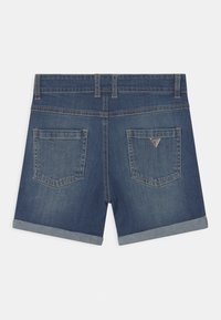 Shorts de denim de color azul oscuro, con puños enrollados y dos bolsillos traseros. Presenta un pequeño logotipo triangular en el bolsillo derecho.