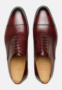 Scarpe da uomo in pelle marrone con punta tondeggiante, sistema di allacciatura e cuciture nere. Texture liscia con una finitura lucida.