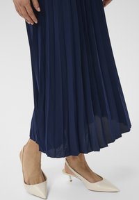 Tengerés pleats szoknya világos bézs slingback sarkakkal, hegyes orral és kis sarokkal. Sima textúra, modern dizájn.
